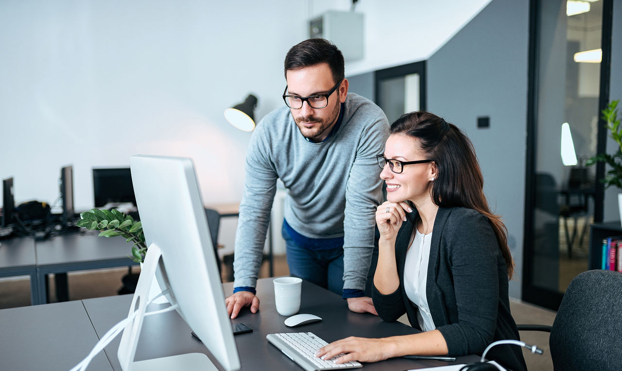 Two young business people looking at computer monitor. Working on a project together.