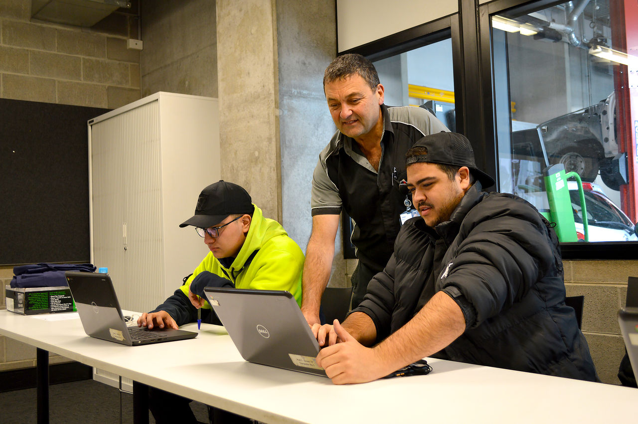 A male teacher helping males students with the laptop